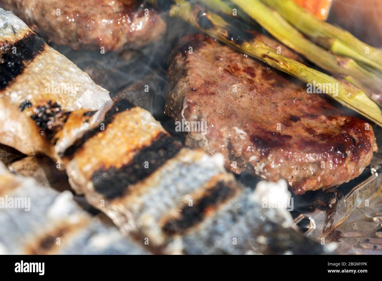 Gegrillte Paprika, Spargel, Würstchen, Burger, gegrillter Fisch. Rosa Lachs, grüner Spargel über Feuer und Rauch. Barbecue im Sommer. Freizeit und f Stockfoto