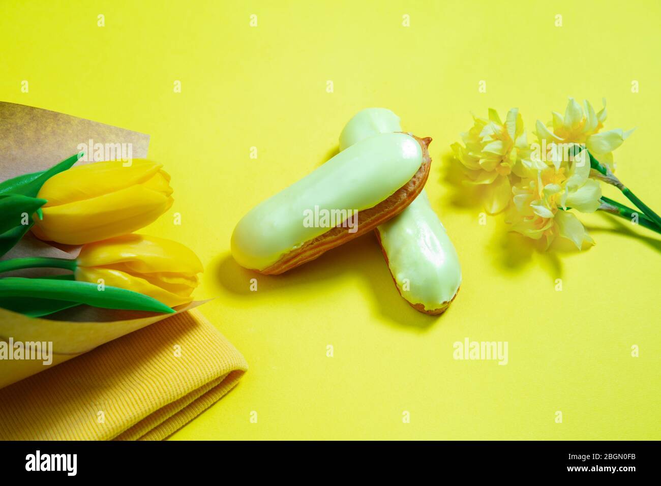 Blumen und Kuchen. Monochrome stilvolle und trendige Komposition in Gelb auf Studio-Hintergrund. Draufsicht, flaches Lay. Reine Schönheit der üblichen Dinge herum. Copyspace für Anzeige. Urlaub, Essen, Mode. Stockfoto