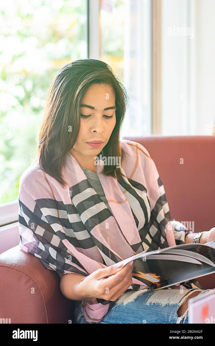 Asiatische Frau war auf dem Sofa lesen Hintergrundfenster mit natürlichem Licht. Stockfoto