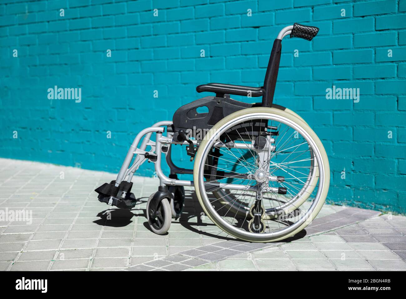 Der Rollstuhl parkte auf der Straße neben der hellblauen Ziegelmauer. Stockfoto