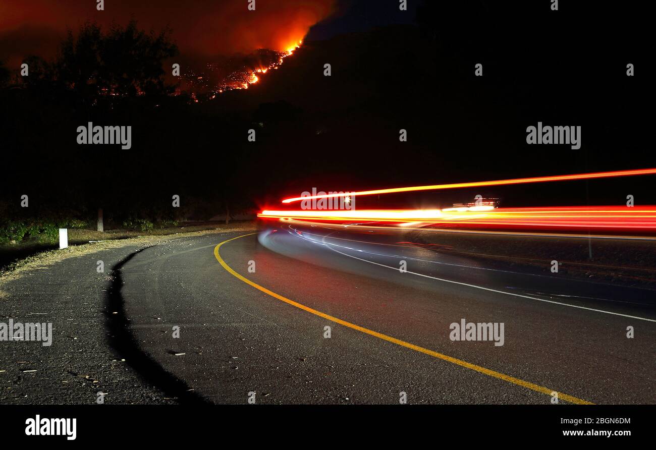 Autoscheinwerfer und Schlussleuchten auf einer Straße mit Bergfeuer im Hintergrund Stockfoto