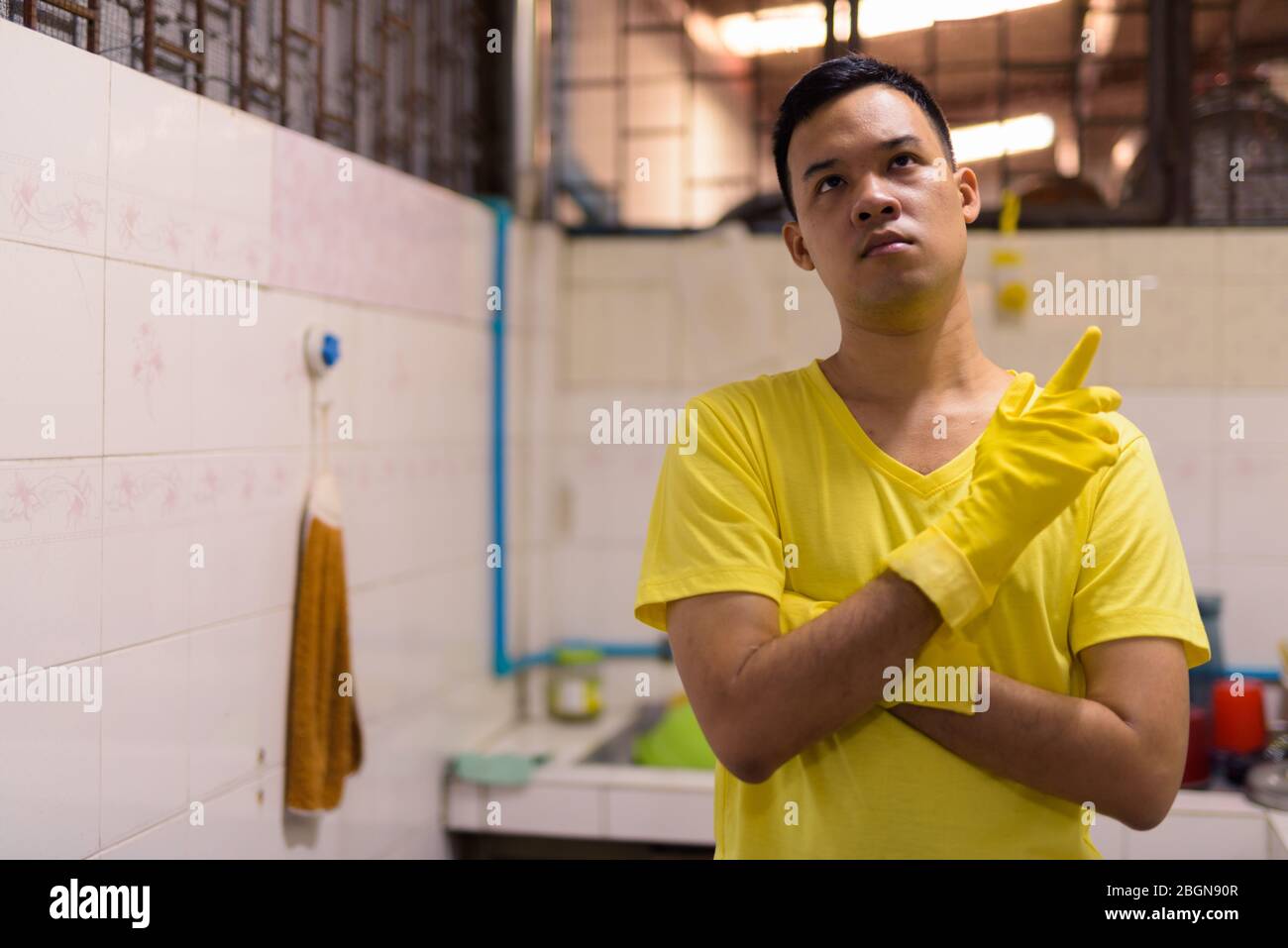 Junge asiatische Mann mit Handschuhen denken und Hausarbeit zu tun Stockfoto