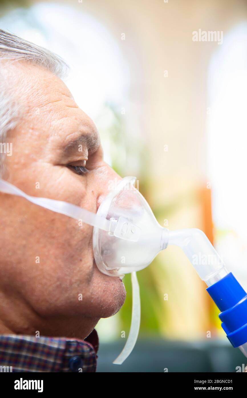 Leitender Mann, der medizinische Geräte für die Inhalation mit Atemschutzmaske verwendet, Vernebler im Zimmer Stockfoto