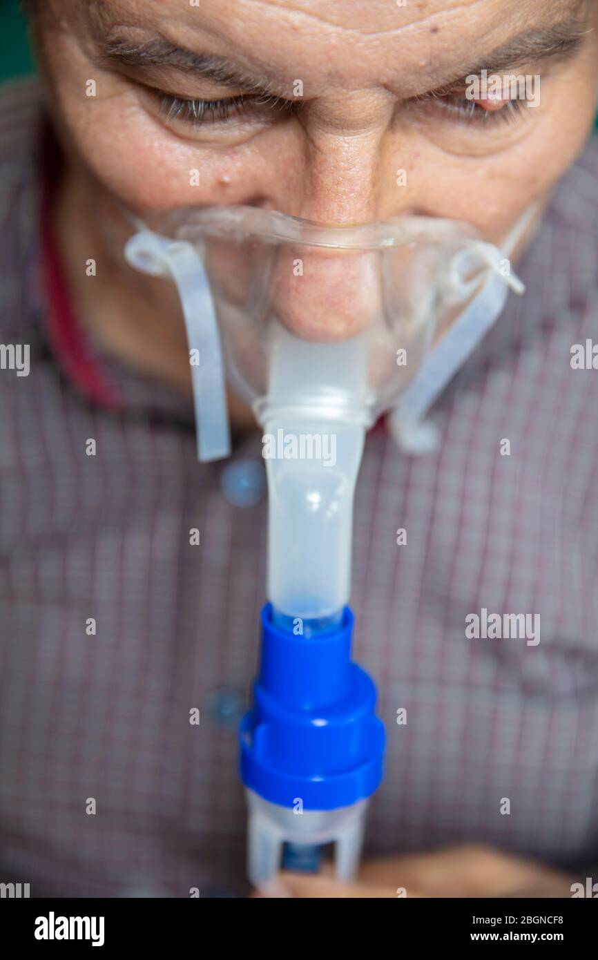 Leitender Mann, der medizinische Geräte für die Inhalation mit Atemschutzmaske verwendet, Vernebler im Zimmer Stockfoto