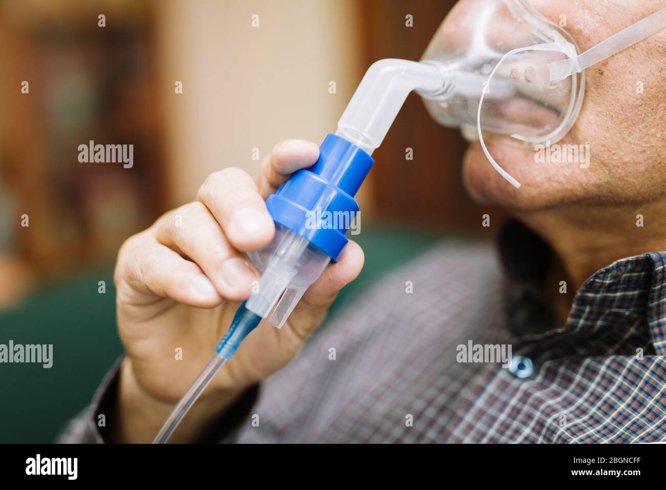 Leitender Mann, der medizinische Geräte für die Inhalation mit Atemschutzmaske verwendet, Vernebler im Zimmer Stockfoto