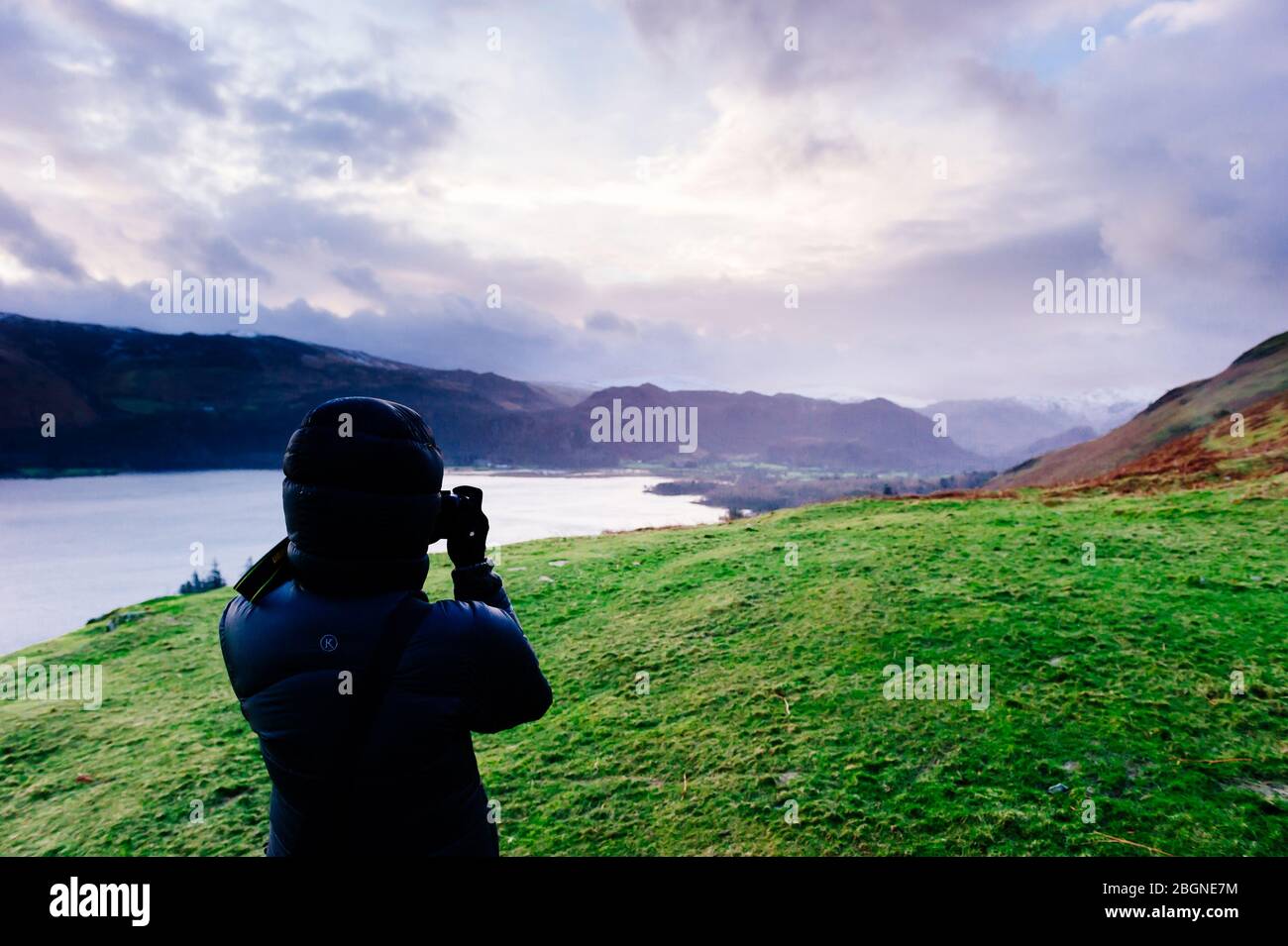 Ein Fotograf hat sich warm in eine Daunenjacke gewickelt und fotografiert den Blick über den Derwent Water Catgells Gipfel mit Blick auf Derwent Water in the Lakes Stockfoto