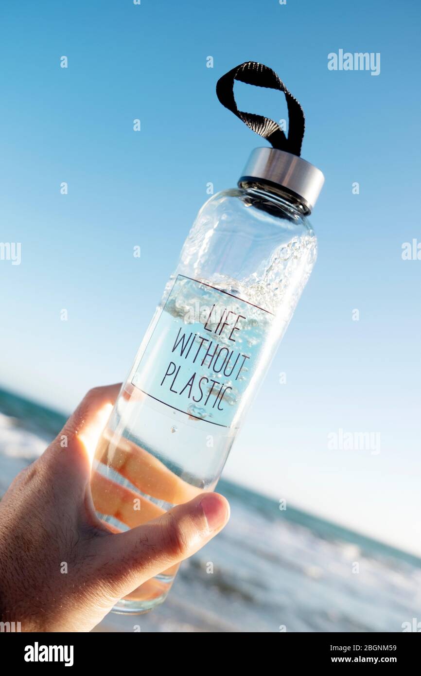 Nahaufnahme von einem kaukasischen Mann hält ein Glas wiederverwendbare Trinkflasche mit dem Text leben ohne Kunststoff in Es geschrieben, am Strand, mit dem Meer in der Stockfoto