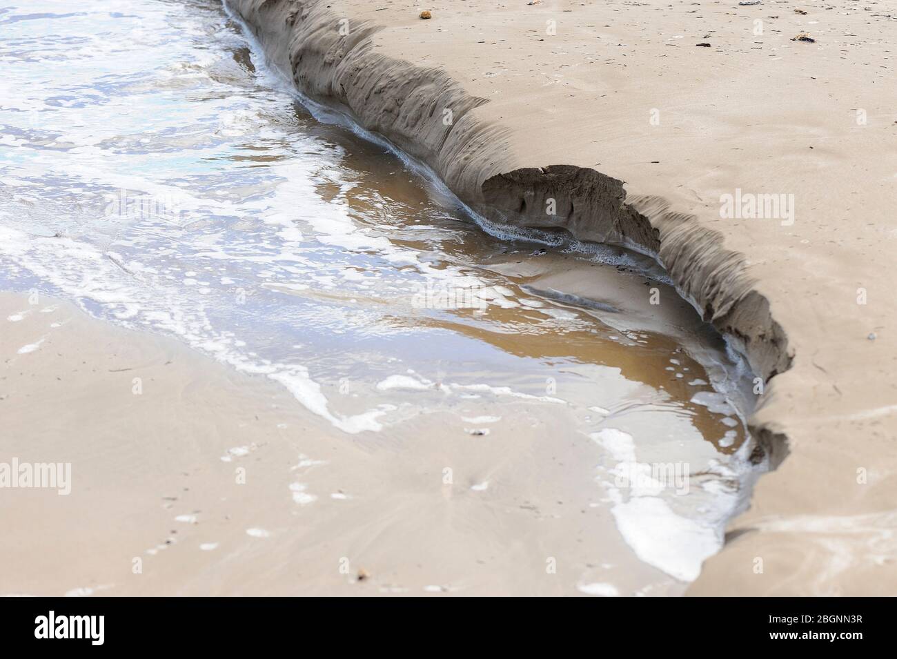 Wellenerosion auf feinem goldenen Strandsand Stockfoto
