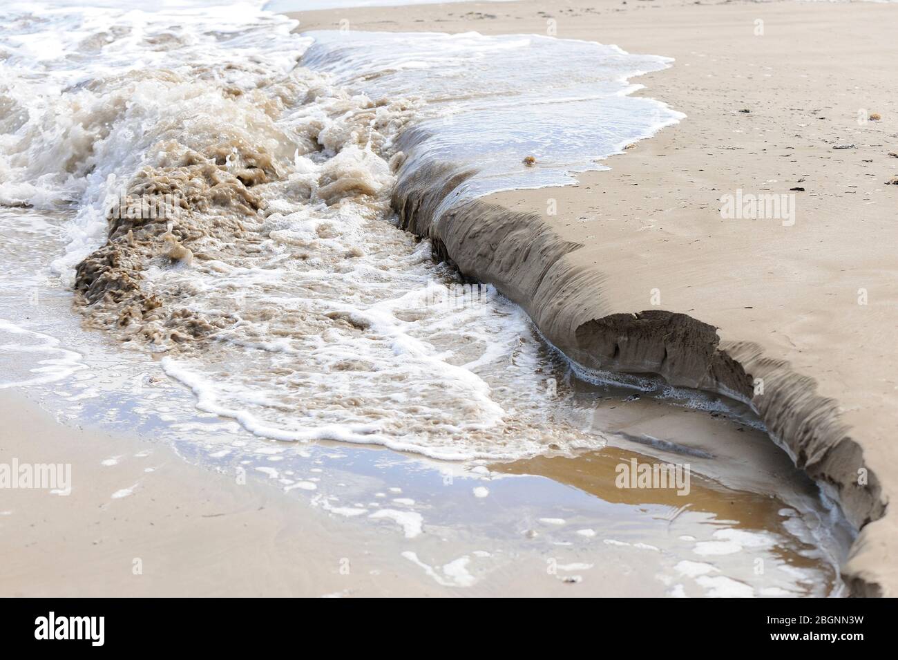Wellenerosion auf feinem goldenen Strandsand Stockfoto