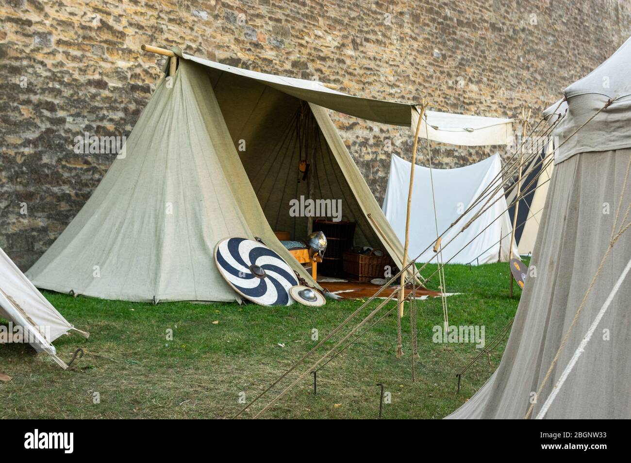 Nachstellung einer mittelalterlichen Szene vor der historischen Kulisse einer alten Stadtmauer, Dorf mit Zelten verschiedener Designs mit Details der Stoffe und Stockfoto