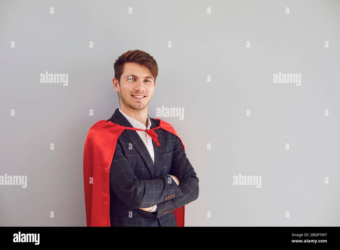 Fröhlicher Mann im Superhelden Kostüm Lächeln auf grauem Hintergrund. Stockfoto