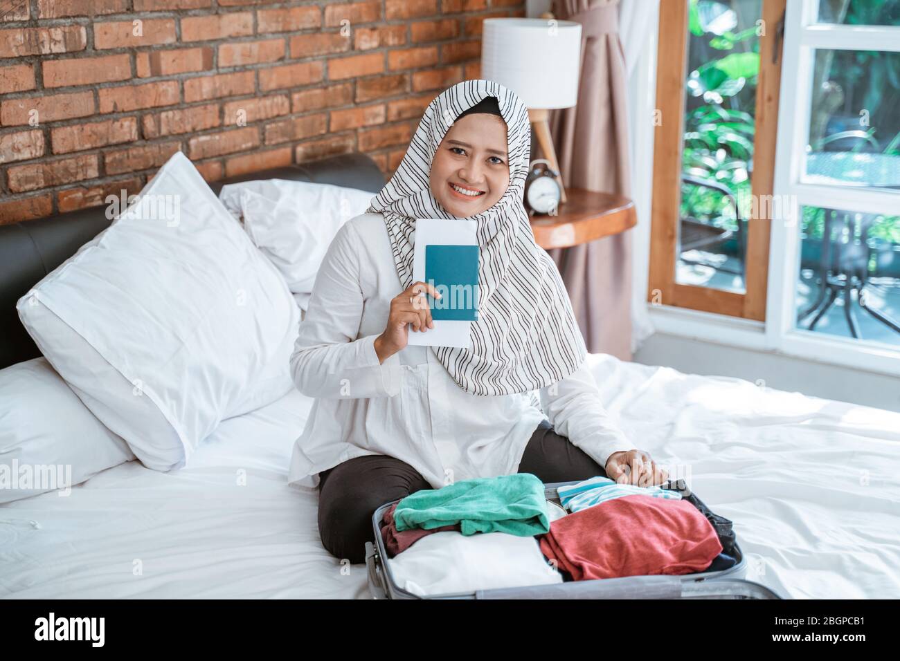 Frau tragen Hijab Vorbereitung für Urlaub halten Reisepass beim Verpacken Stockfoto Frau tragen Hijab Vorbereitung für Urlaub halten Reisepass beim Verpacken Stockfoto