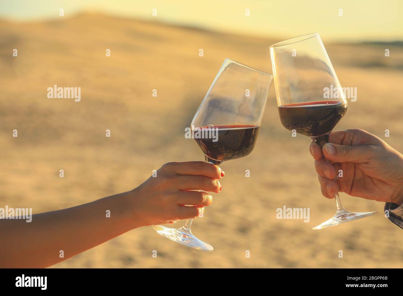 Hände halten Rotweingläser auf Dune von Pyla während des Sonnenuntergangs, Feier Konzept Stockfoto