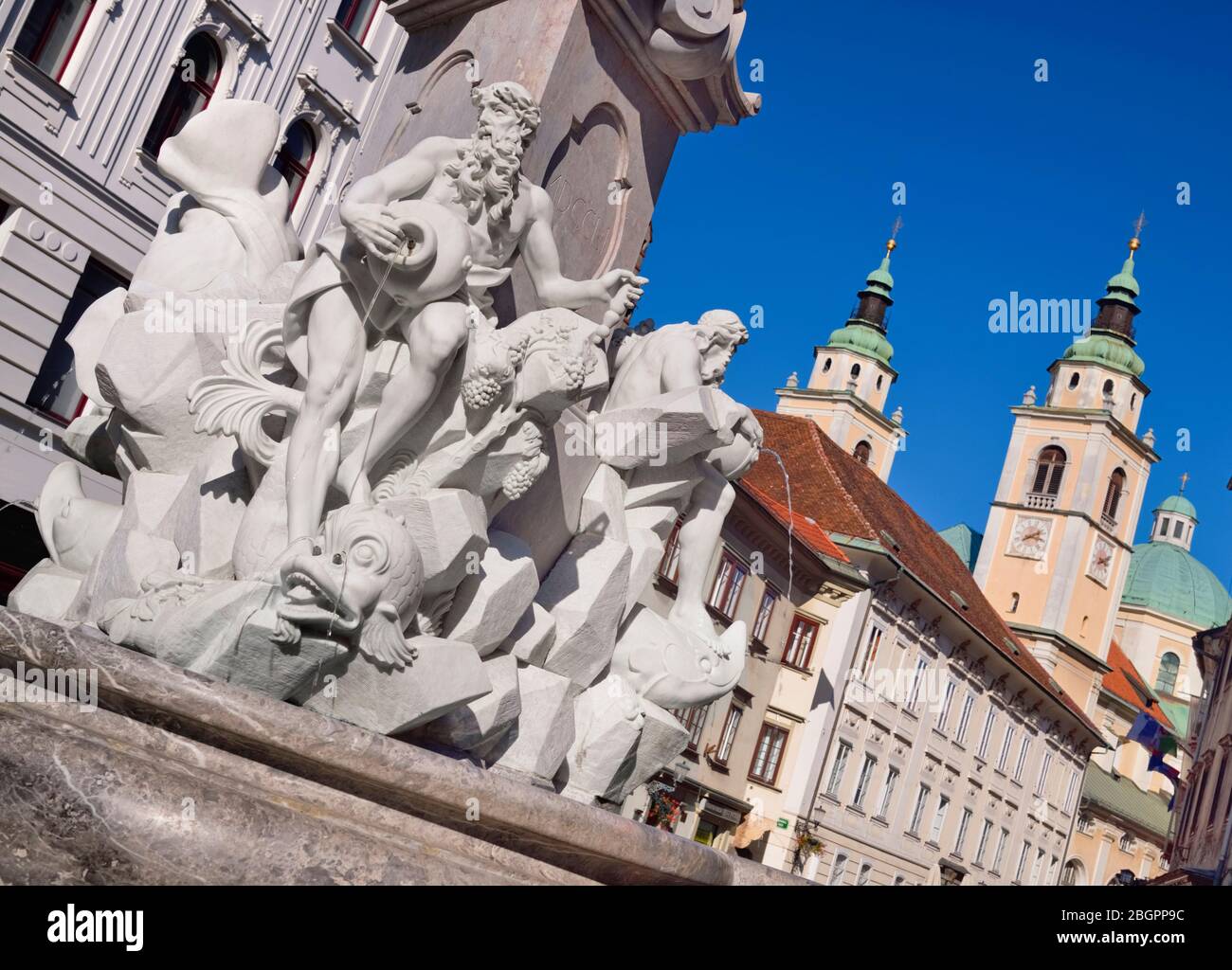 Slowenien, Ljubljana, Nahaufnahme der Figuren auf dem Robba-Brunnen mit Türmen und Kuppel der Nikolaikirche im Hintergrund. Stockfoto