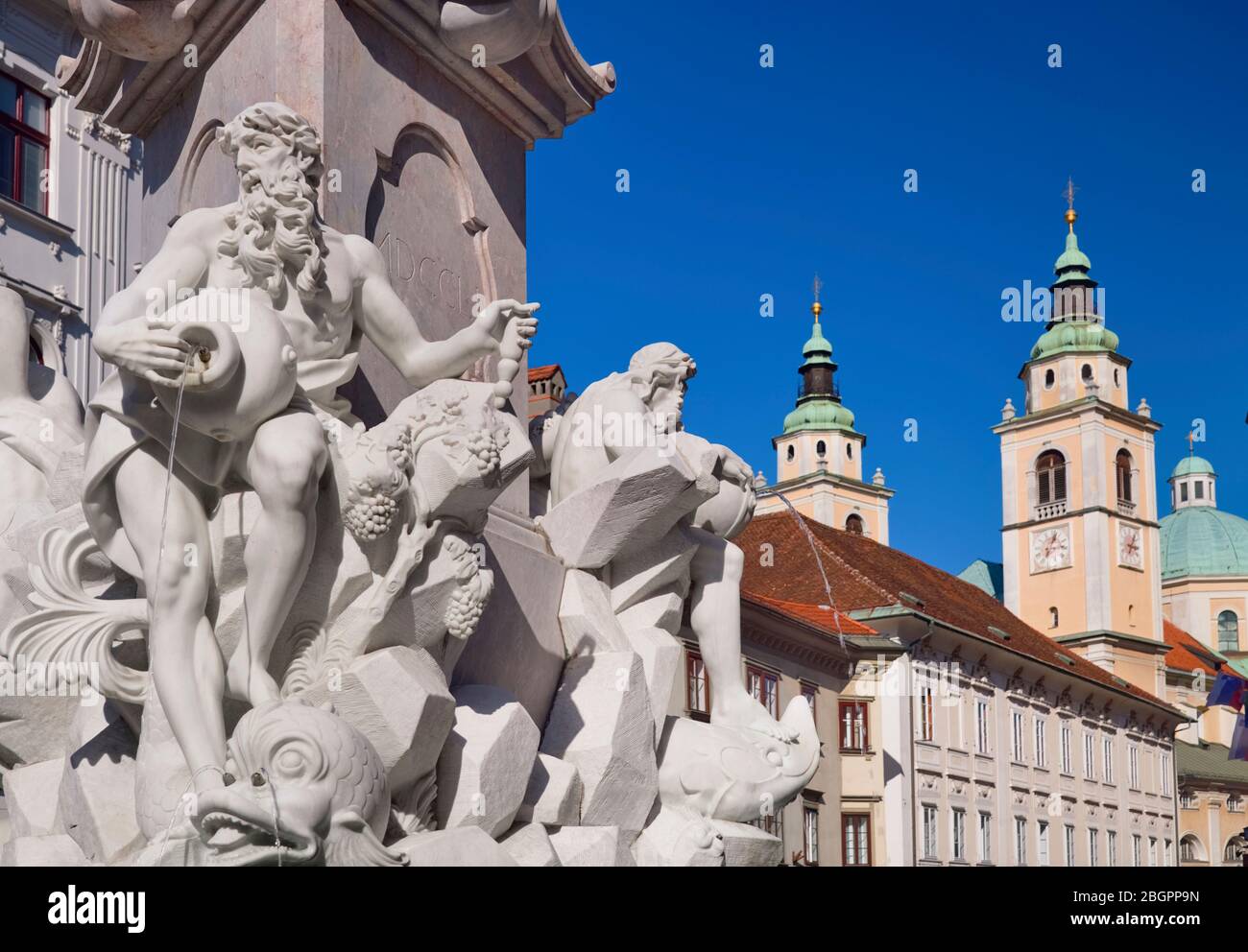 Slowenien, Ljubljana, Nahaufnahme der Figuren auf dem Robba-Brunnen mit Türmen und Kuppel der Nikolaikirche im Hintergrund. Stockfoto