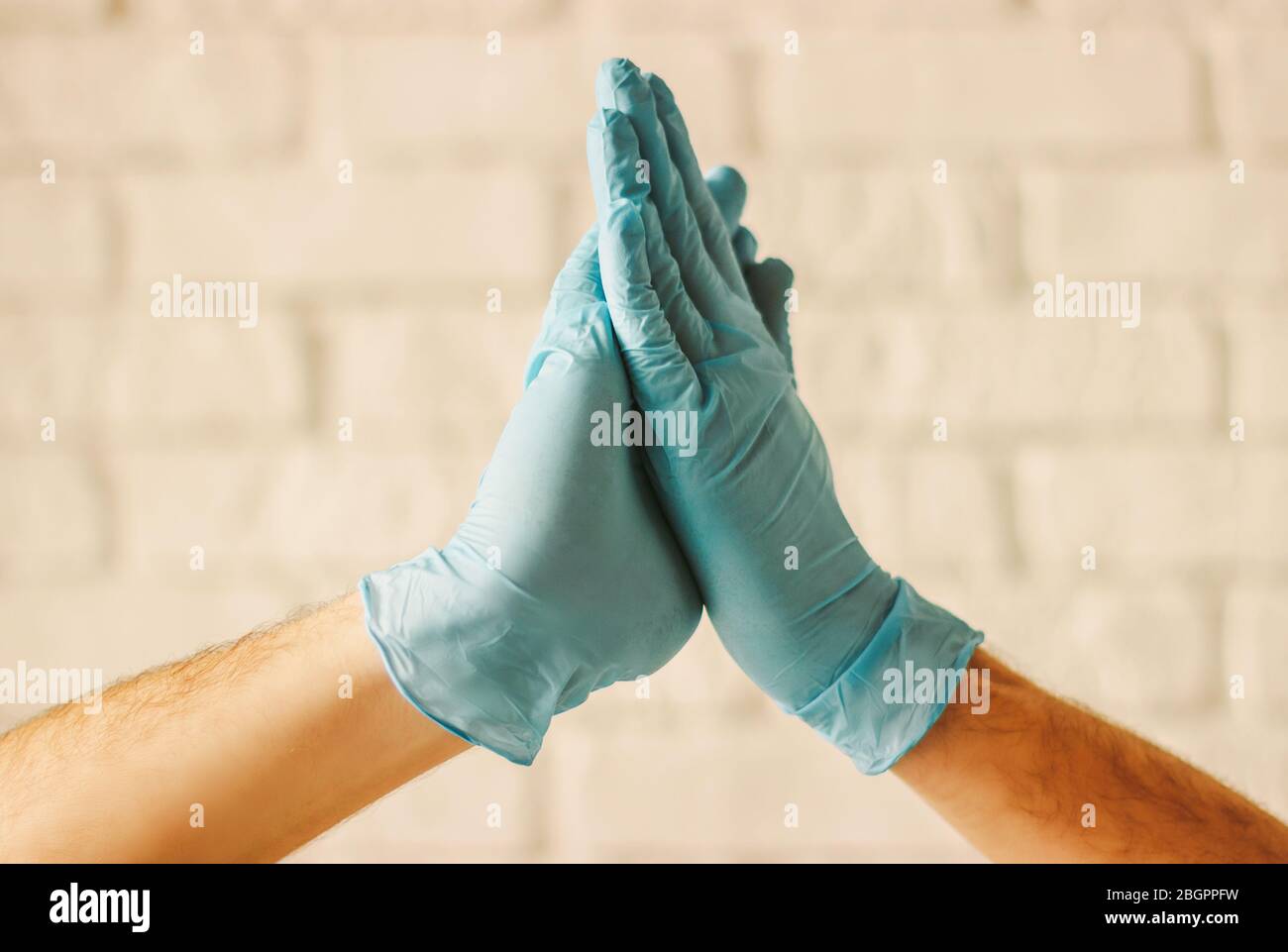 Zwei Männer klatschen mit den Händen in Schutzhandschuhe. Ärzte tragen medizinische Handschuhe an den Händen und feiern den Erfolg im Krankenhaus. Neue Palme Gruß. COVID-19 vorh Stockfoto