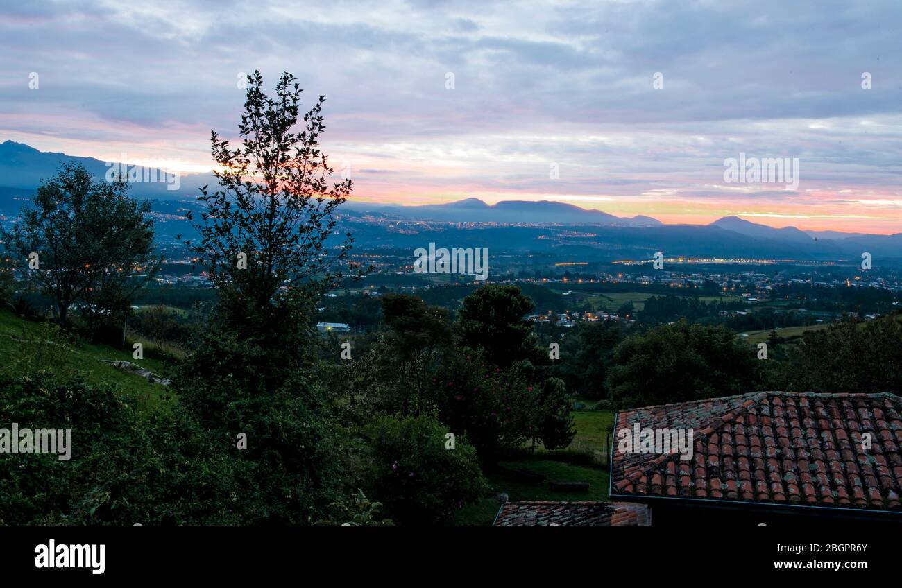 Ein Luftbild der Stadt Quito im Tal bei Sonnenuntergang, von einem der umliegenden Hügel, mit dem Flughafen in der Ferne eingebettet Stockfoto