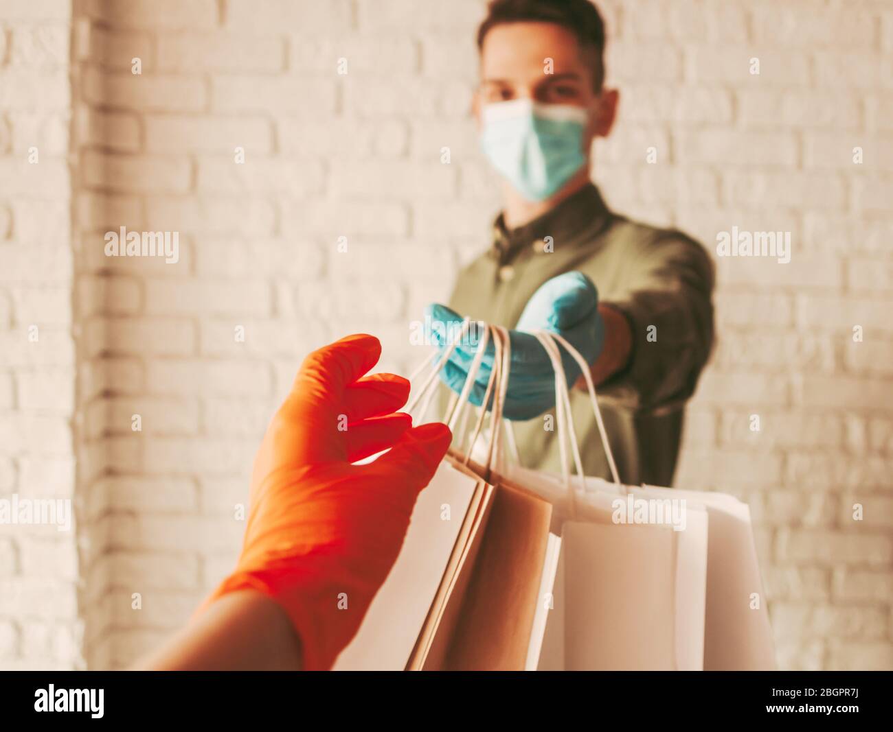 Lieferung Mann Kurier in Schutzmaske und medizinische Handschuhe geben Papiertüten an den Kunden. Mädchen, das Papierpakete erhält. Sichere Online-Lieferung für Stockfoto