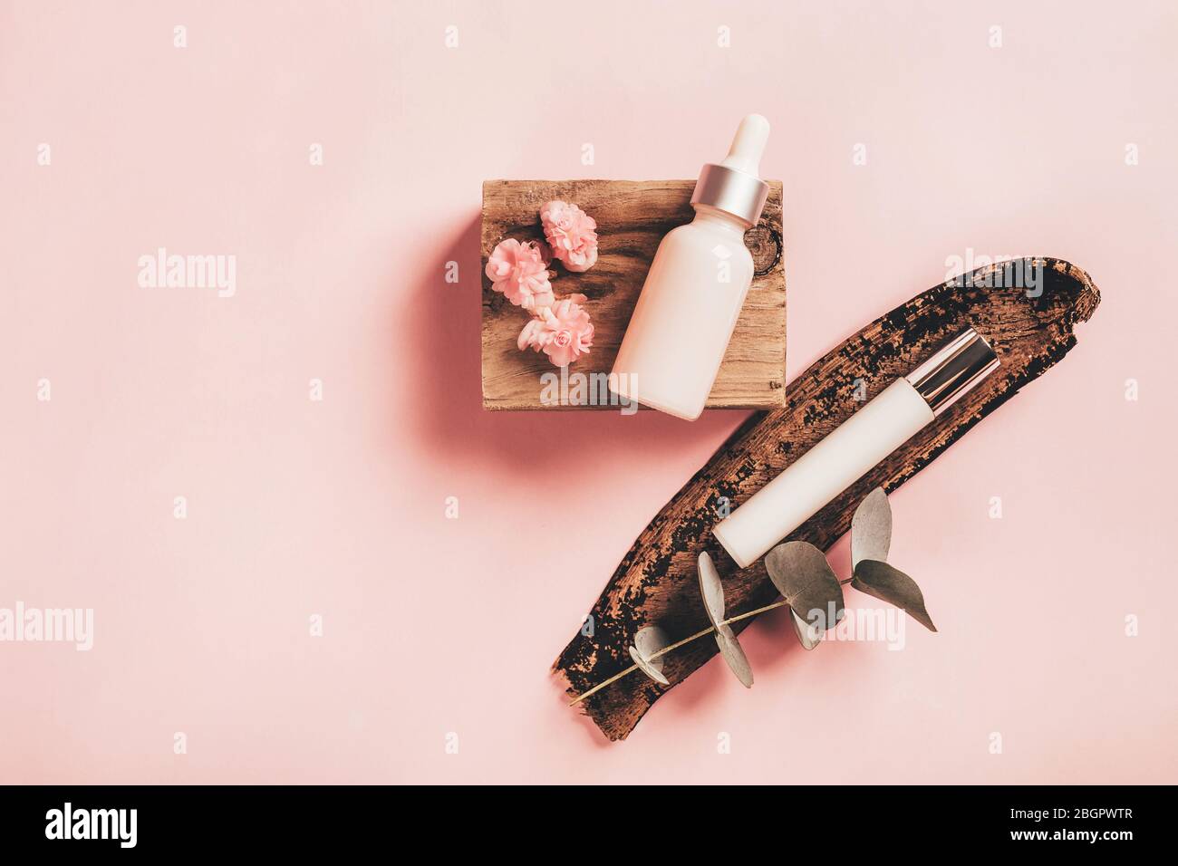 Kosmetikflaschen auf Holzbarren mit Eukalyptus- und Begonia-Blüten auf rosa Papierhintergrund. Gesundheits- und Schönheitskonzept. Stockfoto