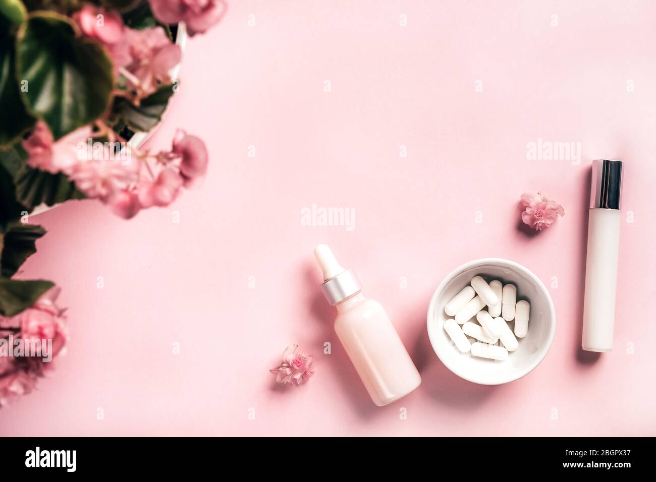 Kosmetikflaschen und weiße Kapseln mit Begonia-Blüten auf rosa Papiergrund. Gesundheits- und Schönheitskonzept. Stockfoto