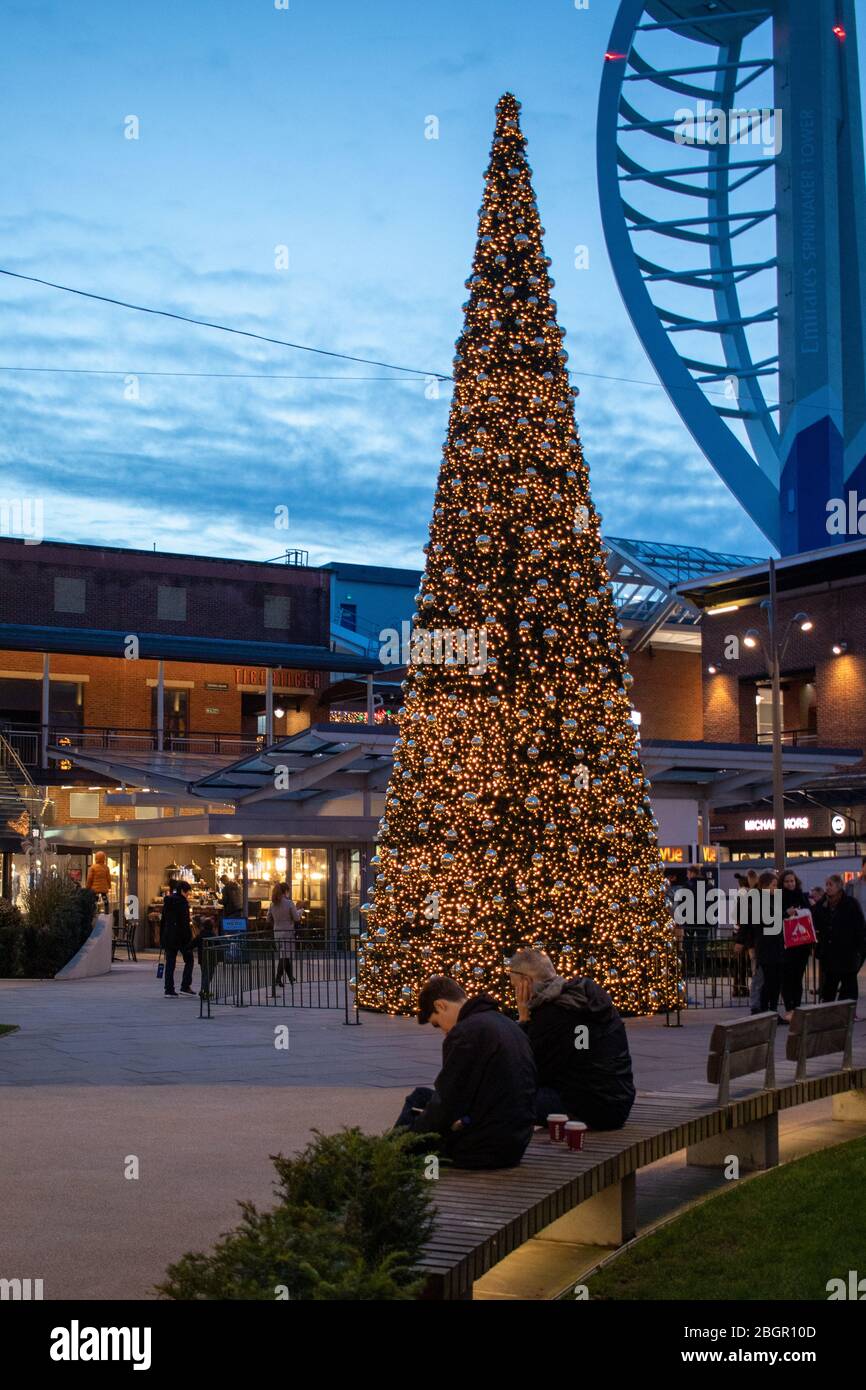 Der Weihnachtsbaum, umgeben von Käufern in Gunwharf Quays, Portsmouth mit dem Spinnaker Tower im Hintergrund Stockfoto