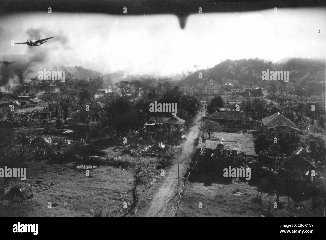 Bomben fallen # 1. Armee Luftwaffe fliegt Bombenangriffe über die hügelige Stadt San Fernando, die Philippinen, c. 1945. Der Blick nach hinten unter einem Flugzeug teilt sich den Luftraum mit einem mittelschweren Bomber, der über San Fernando fliegt. Dieser Bomber hat seine Bombenabwurftür geöffnet und schwerer Staub und Rauch steigen von mehreren Stellen auf dem Boden auf, wo Bomben getroffen haben. Der Bomber scheint entweder ein mittlerer Bomber Douglas A-20 Havoc oder ein mittlerer Bomber Douglas A-26 Invader zu sein. Um meine anderen WW II-bezogenen Bilder zu sehen, Suche: Prestor Vintage WW II Stockfoto