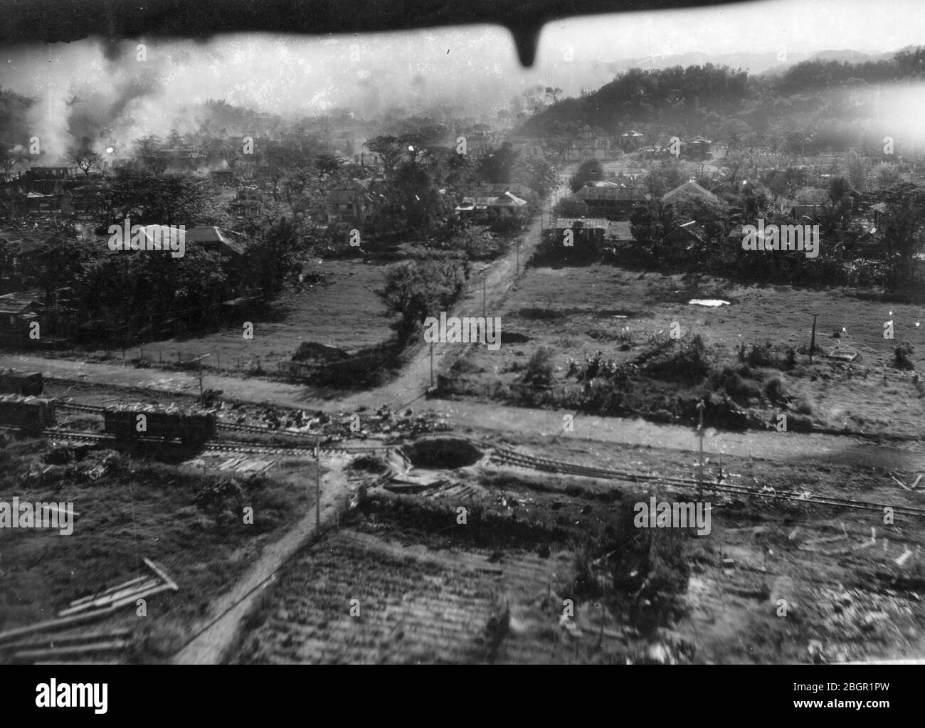 Bomben fallen # 2. Armee Luftwaffe fliegt Bombenangriffe über die hügelige Stadt San Fernando, die Philippinen, c. 1945. Dieser Blick nach hinten folgt dem vorherigen Foto, das die Landschaft etwa 100 Meter weiter vom Dorf zeigt. Diese Luftaufnahme zeigt zahlreiche Bombenkrater, darunter einen perfekten direkten Treffer auf den Eisenbahnschienen der Stadt. Mehr Staub und Rauch steigen vom Boden auf, wo Bomben getroffen haben. Um meine anderen WW II-bezogenen Bilder zu sehen, Suche: Prestor Vintage WW II Stockfoto