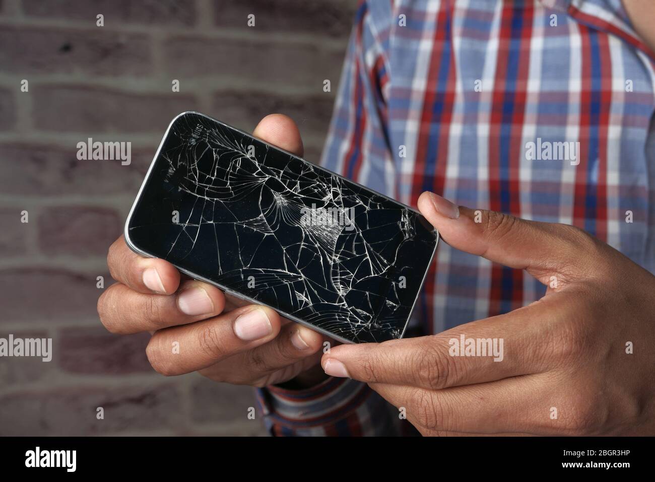 Nahaufnahme der Hand des Mannes, der ein gebrochenes Smartphone hält Stockfoto