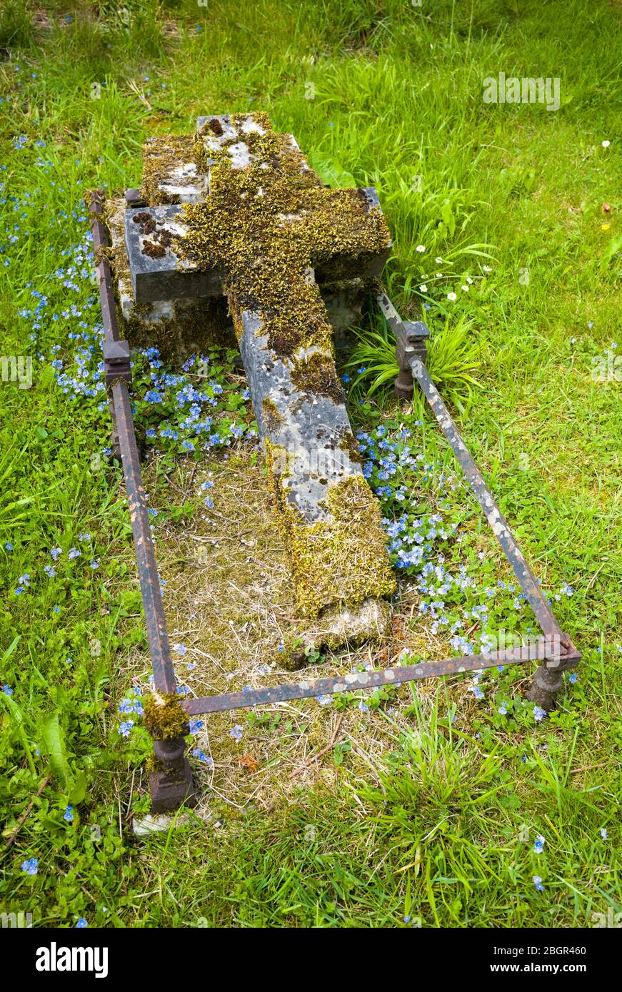 Ein altes moosbedecktes Kreuz auf einem Grab in einem traditionellen Kirchfriedhof in England Stockfoto