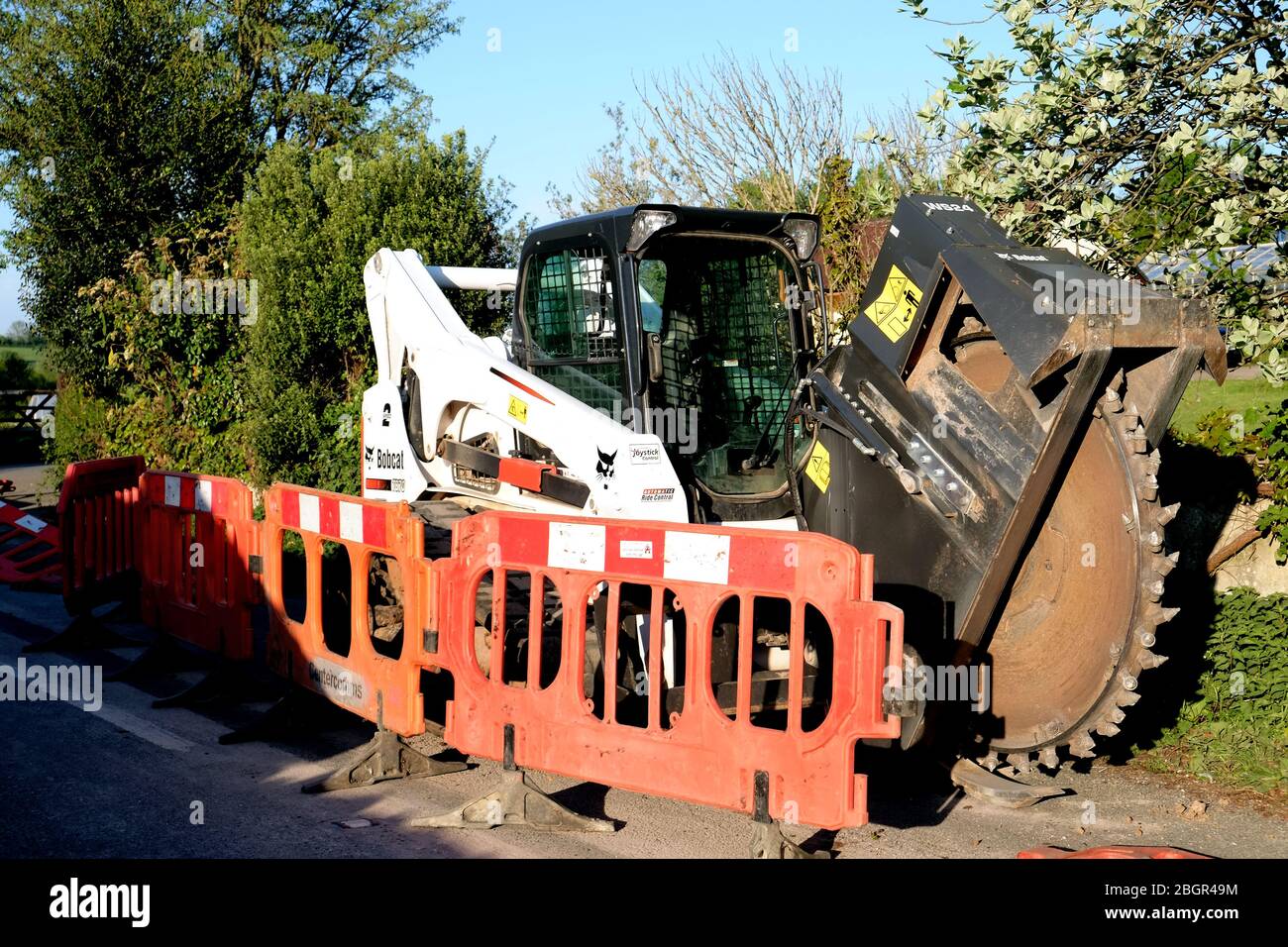 April 2020 - Bobcat-Schlittenlenker-Lader auf Schienen, die mit einem Grabenrad verwendet werden, um Kanäle für Datenkabel im ländlichen Somerset zu verlegen Stockfoto