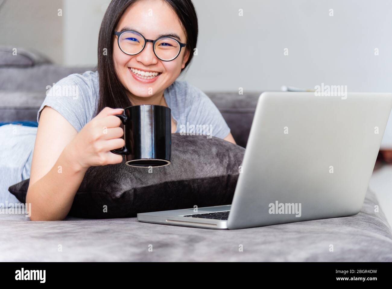 Porträt schöne asiatische junge Frau hält Kaffeetasse Lächeln und suchen während einer Arbeit, nettes Mädchen Teens glücklich auf dem Sofa arbeiten Remote mit einem Schoß Stockfoto