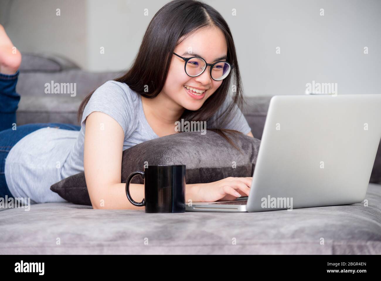 Porträt schöne asiatische junge Frau liegen entspannen Arbeit mit einem Laptop, nette Mädchen Teens Blick auf den Monitor lächeln glücklich auf dem Sofa arbeiten entfernt Stockfoto