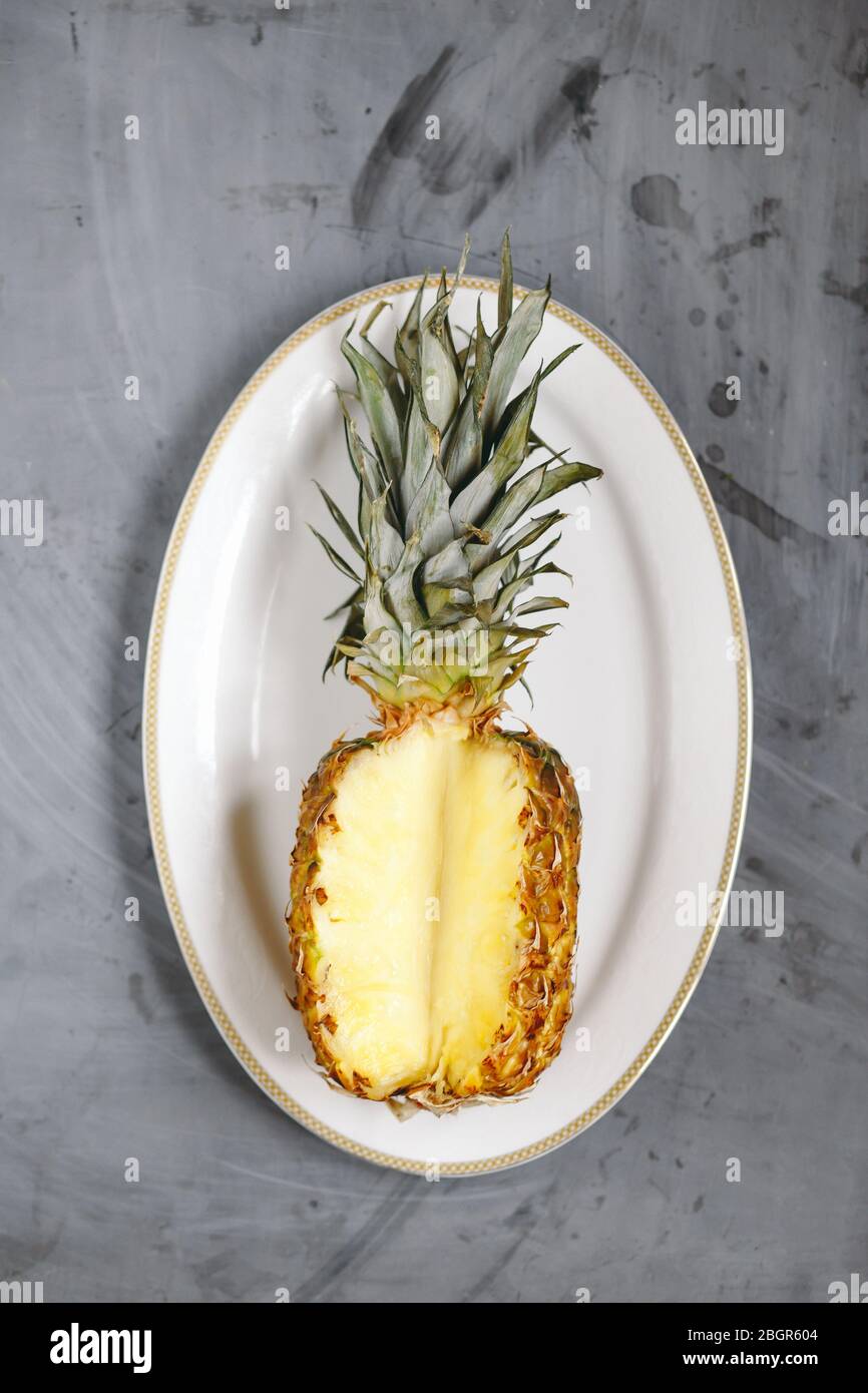 Weißer Teller mit reifer Ananas in Scheiben auf grauem Betongrund Stockfoto