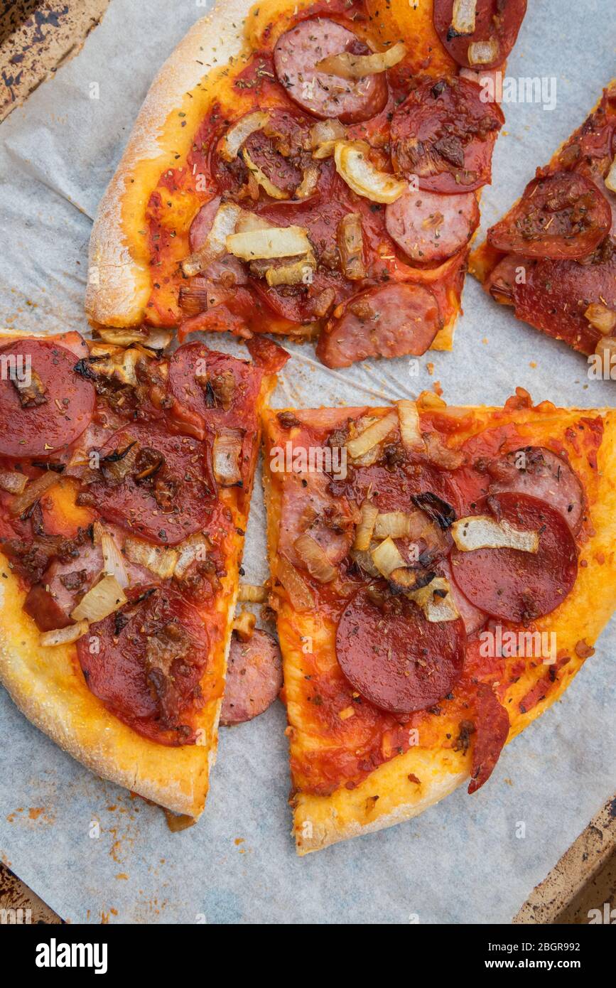 Milchfreie, rustikale Pizza mit dünner Kruste, die aus eigener Herstellung mit Pfefferoni, Speck, Bauernwurst und karamellisierten Zwiebeln zubereitet wird Stockfoto