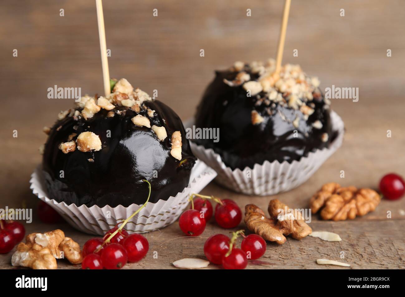 Süße Karamelläpfel auf Stäbchen mit Beeren, auf Holztisch Stockfoto