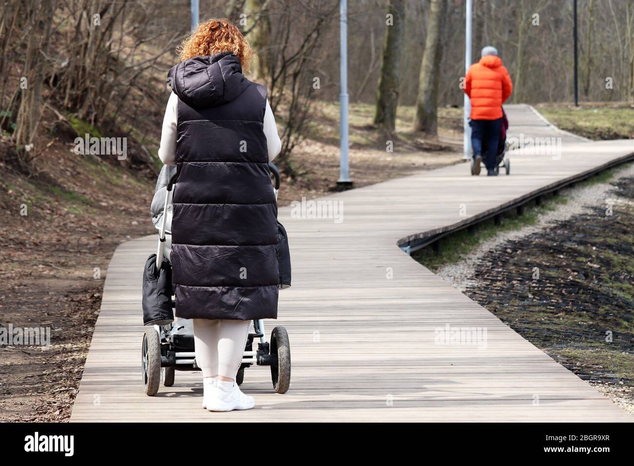 Frau mit einem Kinderwagen zu Fuß im Frühlingspark. Quarantäne in einer Stadt während Covid-19 Coronavirus Pandemie, Konzept der Mutterschaft, Menschen mit Kinderwagen Stockfoto