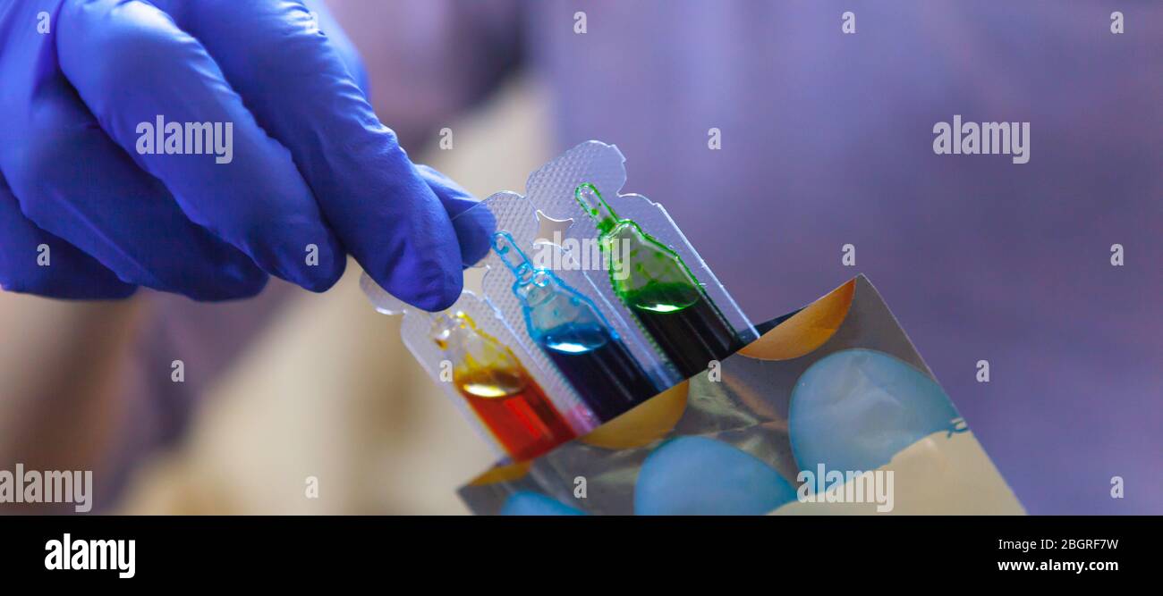 Weibliche Hand in einem blauen Handschuh mit Ampullen von farbigen Farbe zum Anmalen von Ostereiern Stockfoto