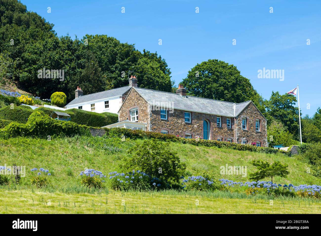 Traditionelles Steintrikot Langhaus mit Agapanthus im Vordergrund in Grouville, Jersey, Channel Isles Stockfoto