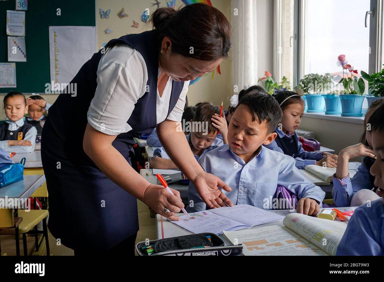 Der Lehrer Nyamtseren Chuluun hilft einem Schüler der dritten Klasse bei seiner Mathearbeit in Ulaanbaatar, Mongolei. Nyamtseren hat über 40 Studenten in ihrer Klasse, was es schwierig für sie macht, jedem einzelnen Aufmerksamkeit zu schenken. (Myagmarsuren Battur, GPJ Mongolei) Stockfoto