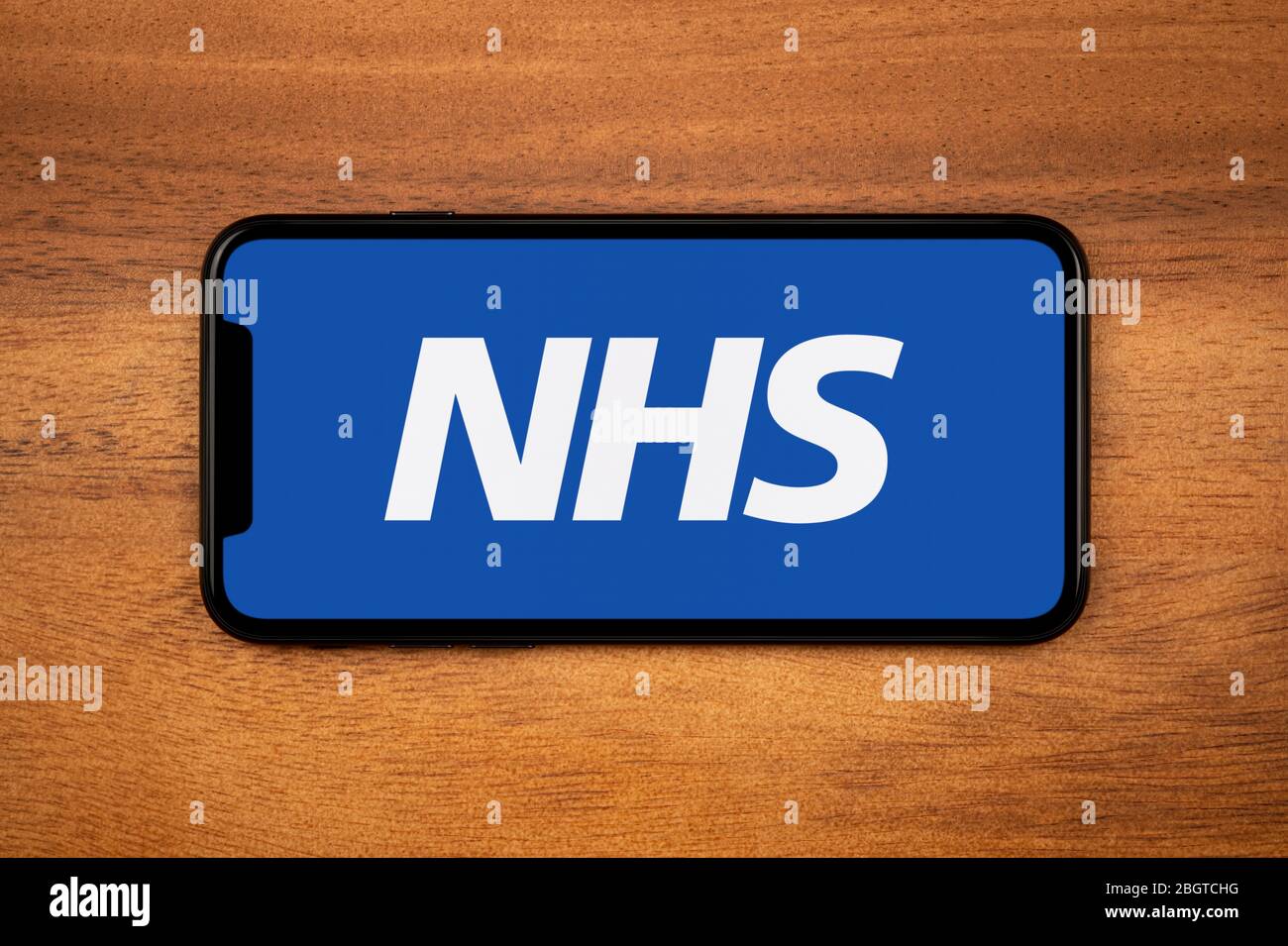 Ein Smartphone mit dem NHS-Logo liegt auf einem einfachen Holztisch (nur für redaktionelle Zwecke). Stockfoto