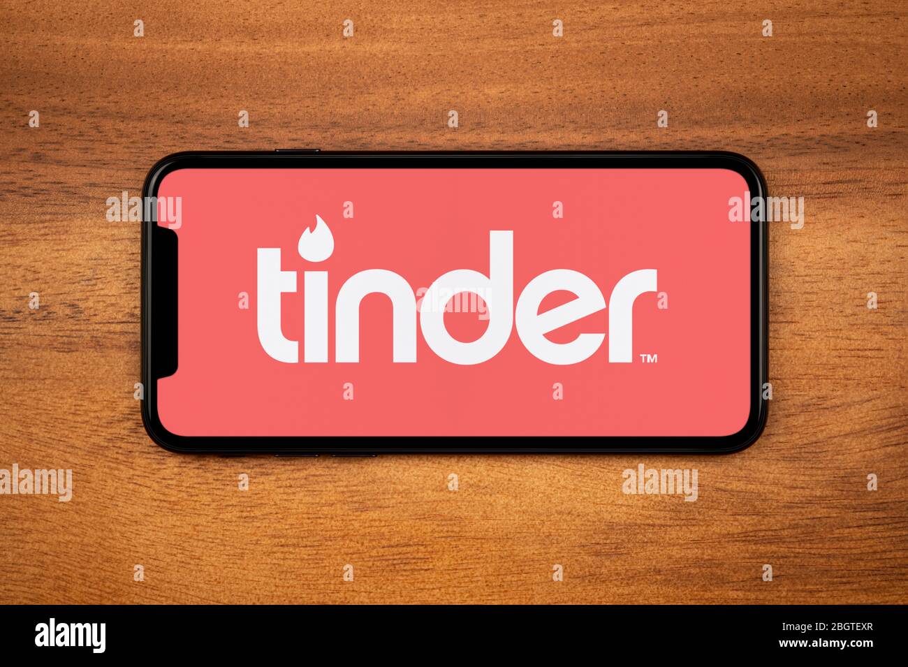 Ein Smartphone mit dem Tinder-Logo liegt auf einem einfachen Holztisch (nur für redaktionelle Zwecke). Stockfoto