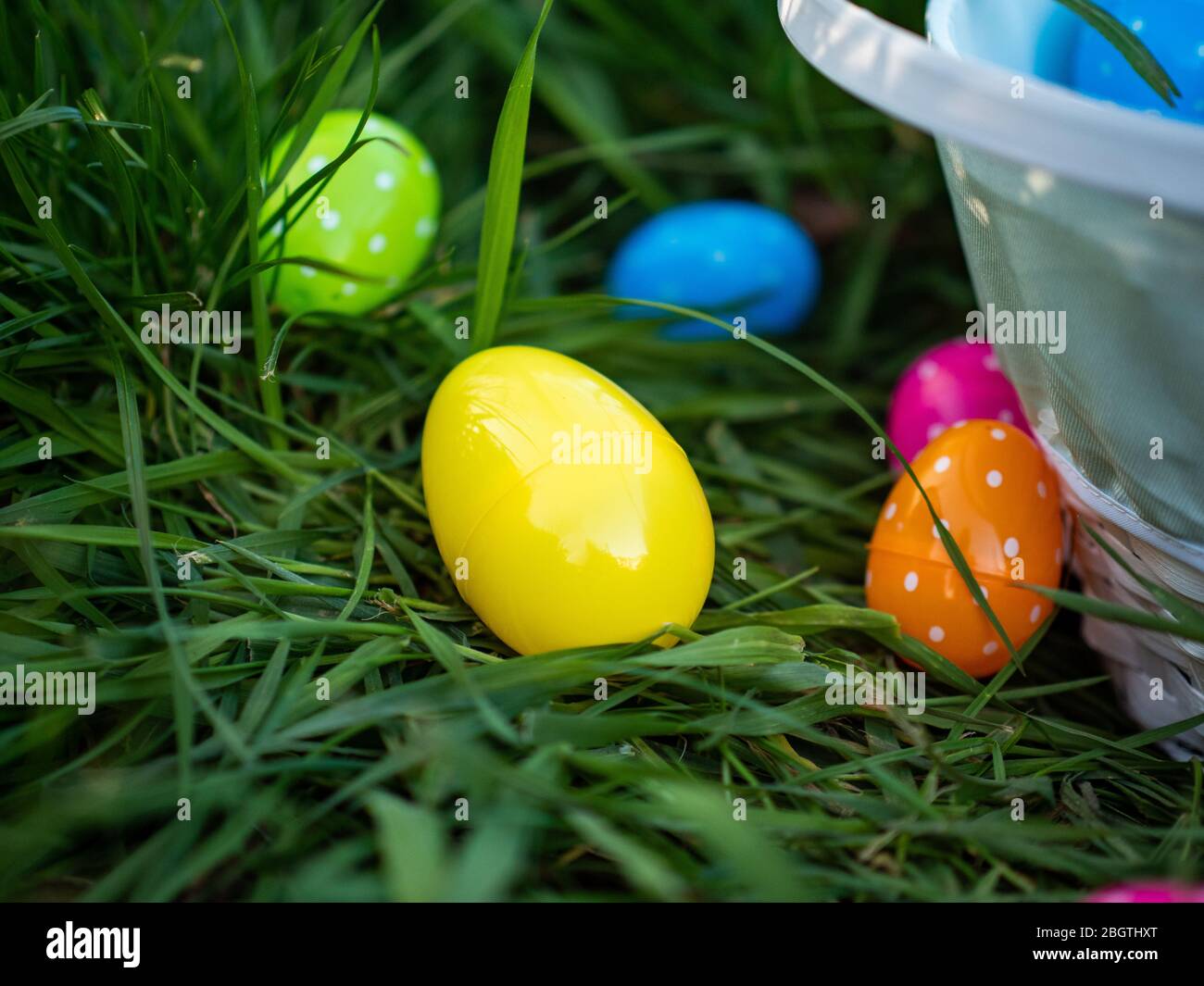 Bunte Ostereier im Gras neben einem Korb voller Polka punktierten Eiern Stockfoto