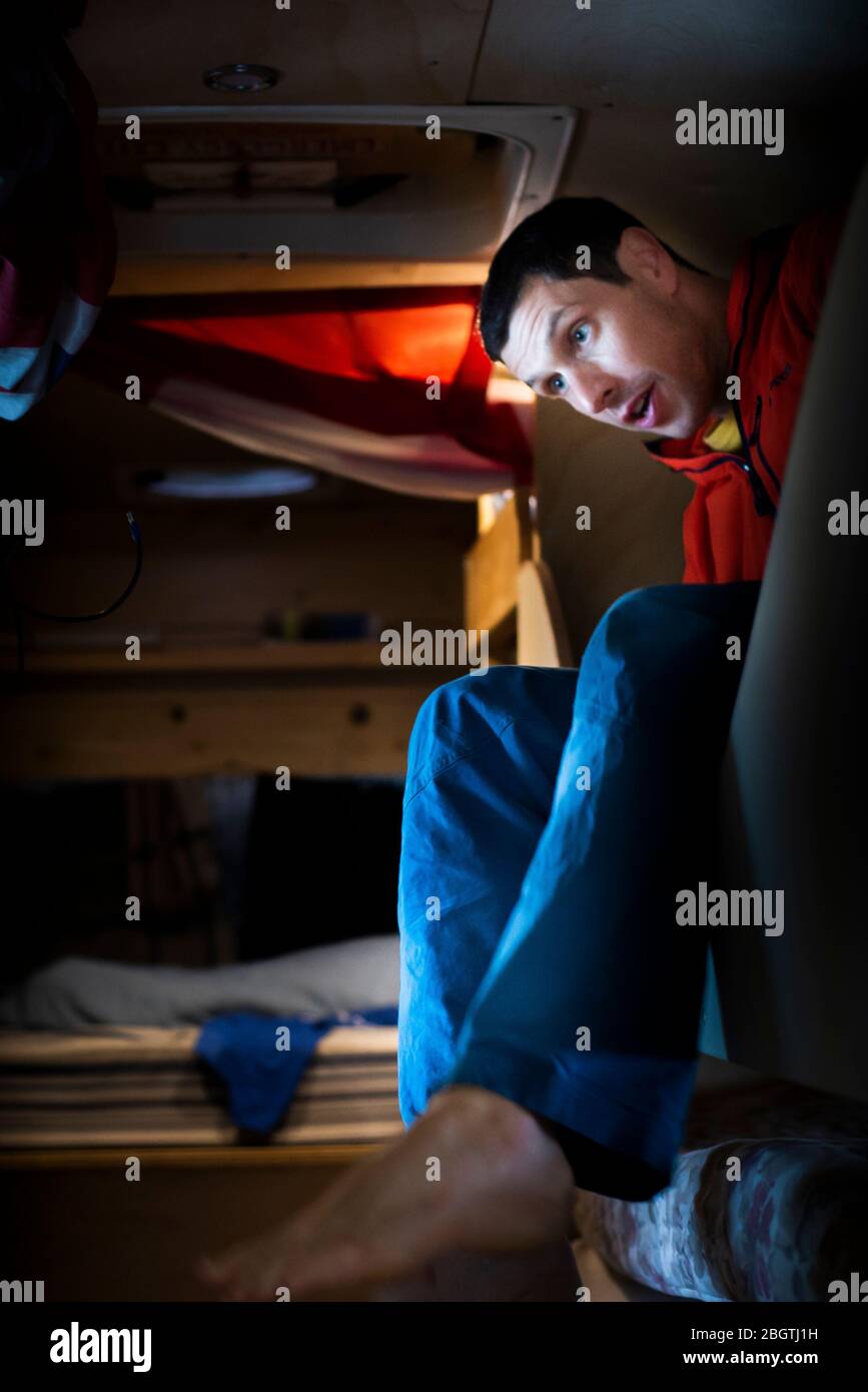 Mann, der aus einem Etagenbett im umgebauten Schulbus aufwacht, verkleidet Stockfoto