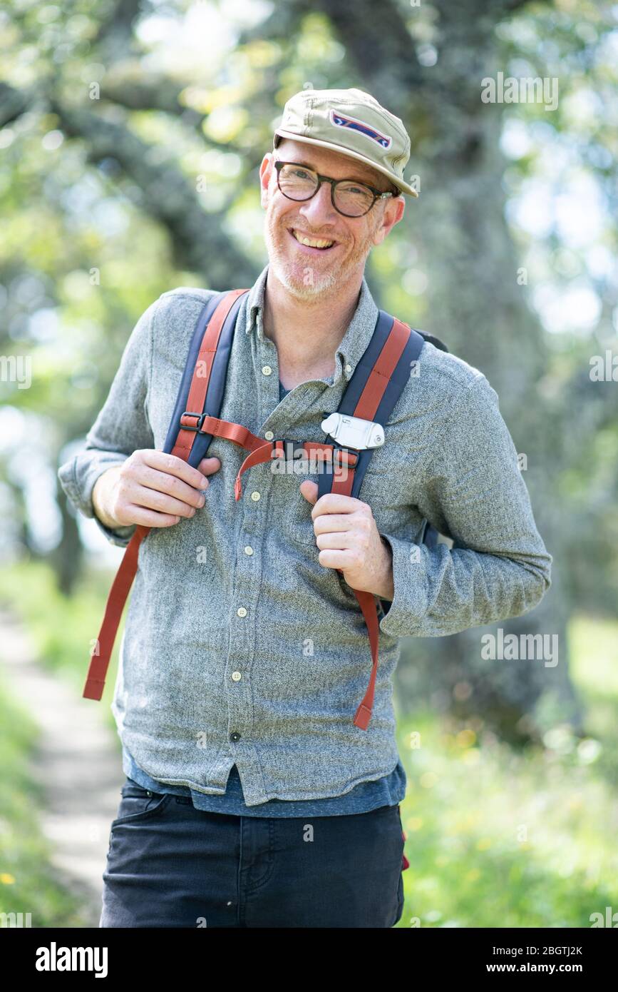 Portrait des lächelnden Wanderers mit Hut, Brille und Rucksack im Freien Stockfoto