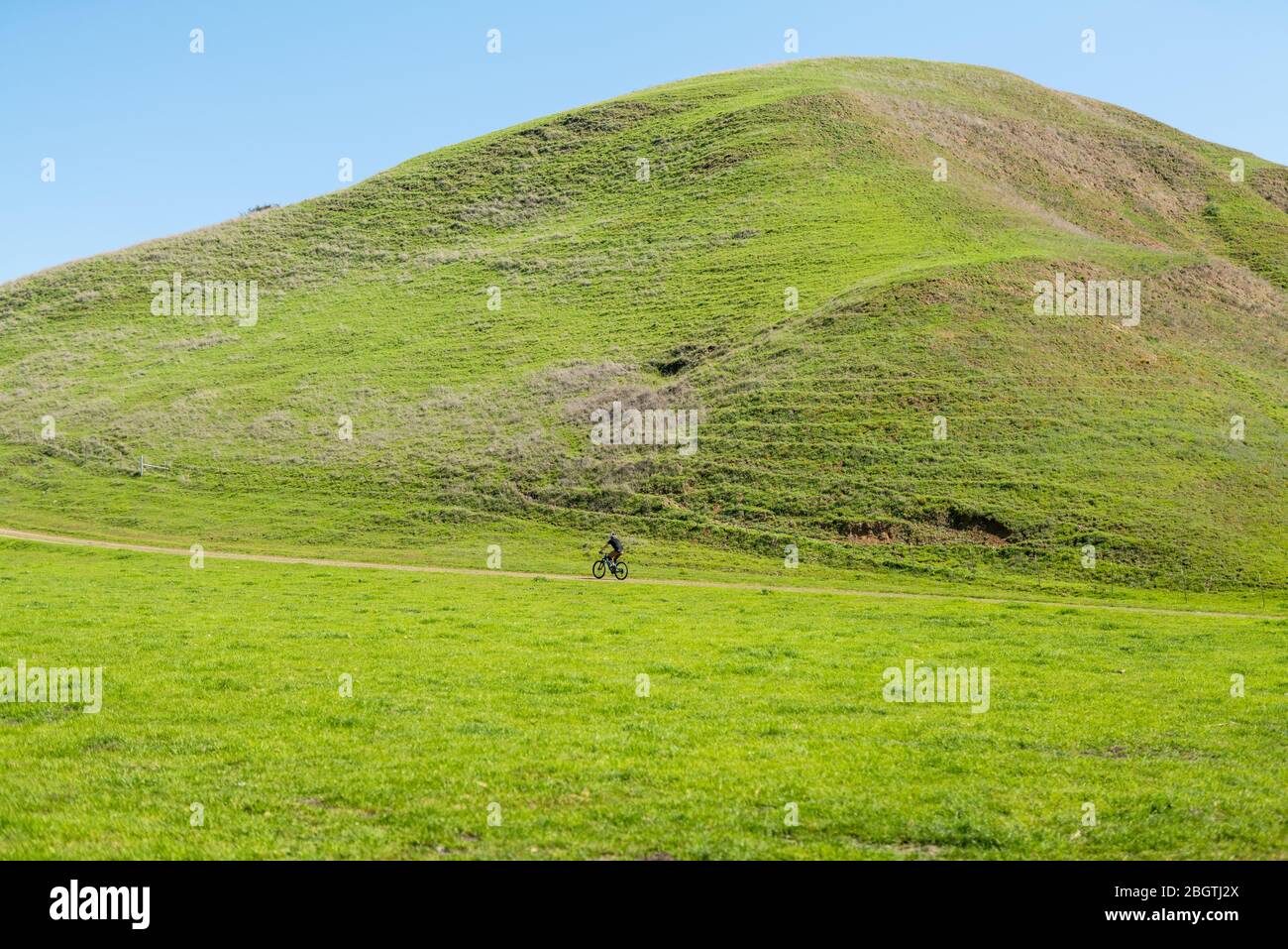 Single Mountain Biker auf entfernten Weg vor grünen Hügeln Stockfoto