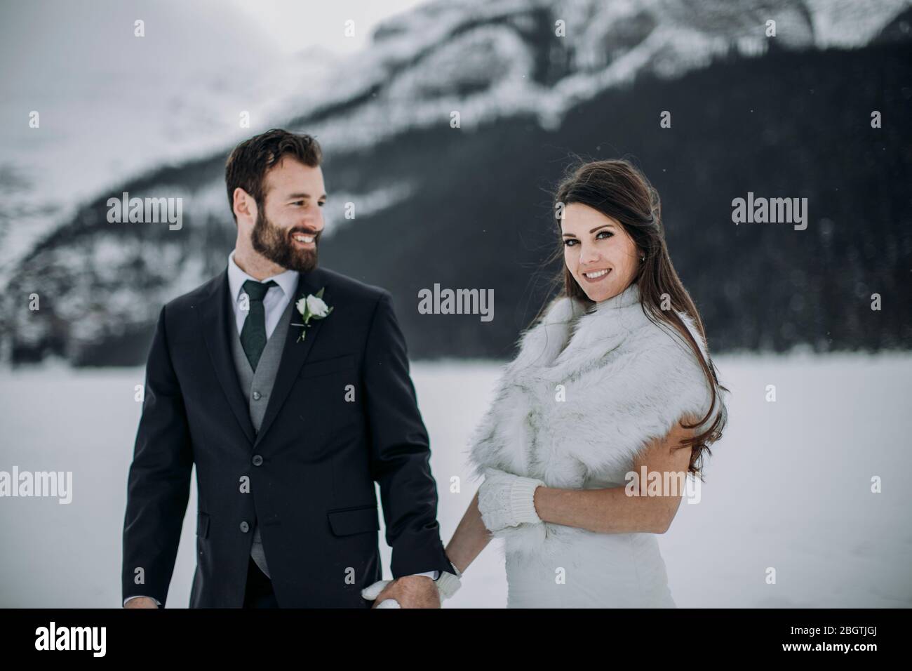 Bräutigam im Anzug blickt auf frisch verheiratete Frau im weißen Hochzeitskleid Winter Stockfoto