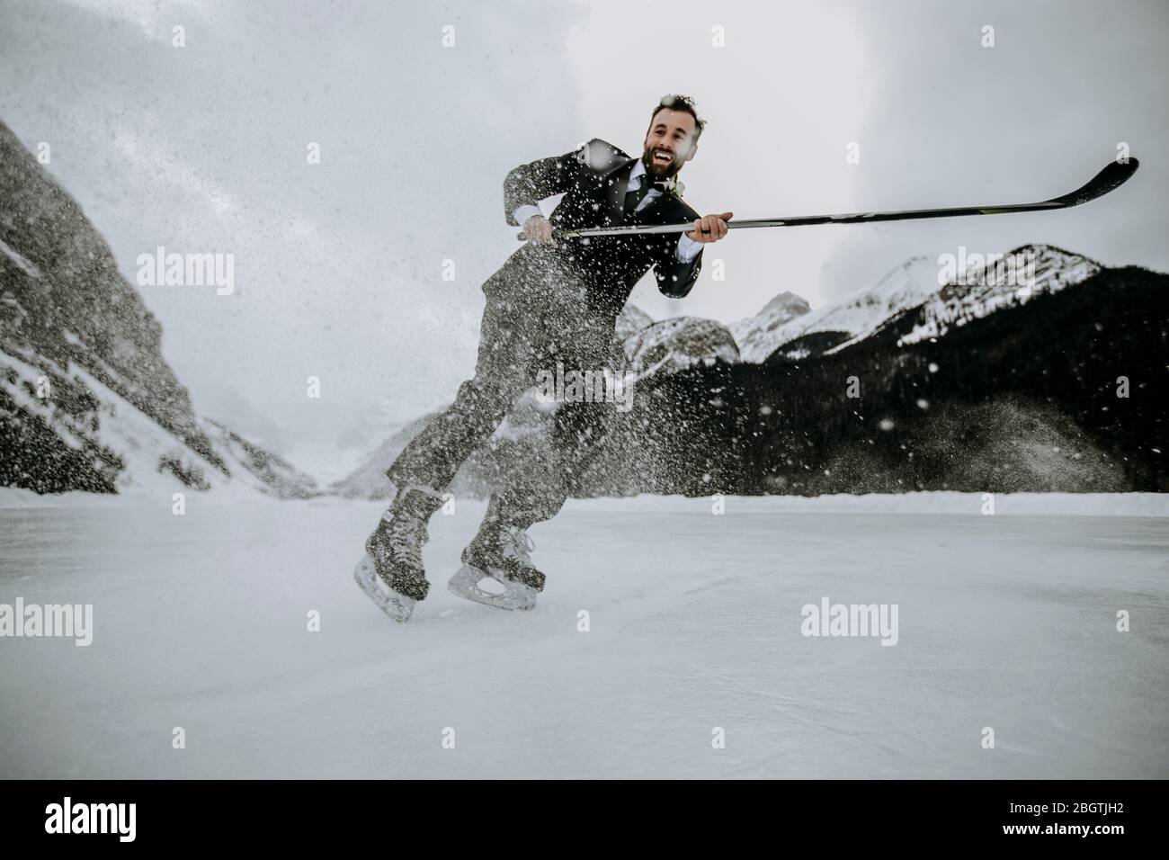 Lächelnder Hockeyspieler im Anzug hält schnell am gefrorenen Lake Louise an Stockfoto