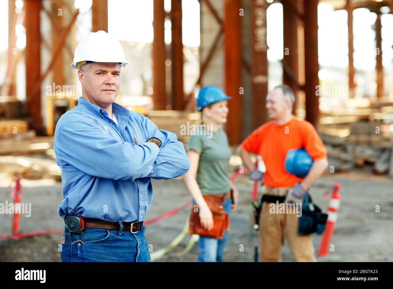 Porträt des männlichen Bauvorarbeiters mit zwei Arbeitern dahinter Stockfoto