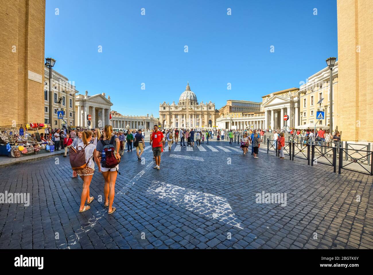 Zwei junge Damen mit Rucksäcken fahren an einem sonnigen Tag in der Vatikanstadt auf die Piazza San Pietro und den Petersdom Stockfoto