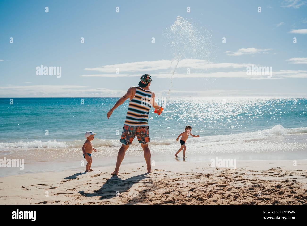 Kinder spielen mit Wasser am Strand mit ihrem Vater an einem sonnigen Tag Stockfoto